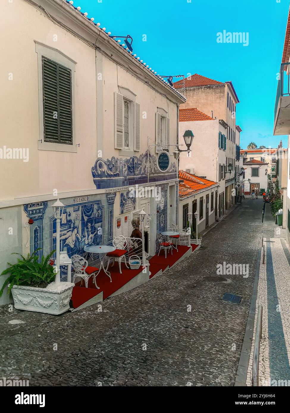 Affascinante strada acciottolata con posti a sedere all'aperto e piastrelle blu azulejo sulla facciata di un caffè a Madeira. Foto Stock