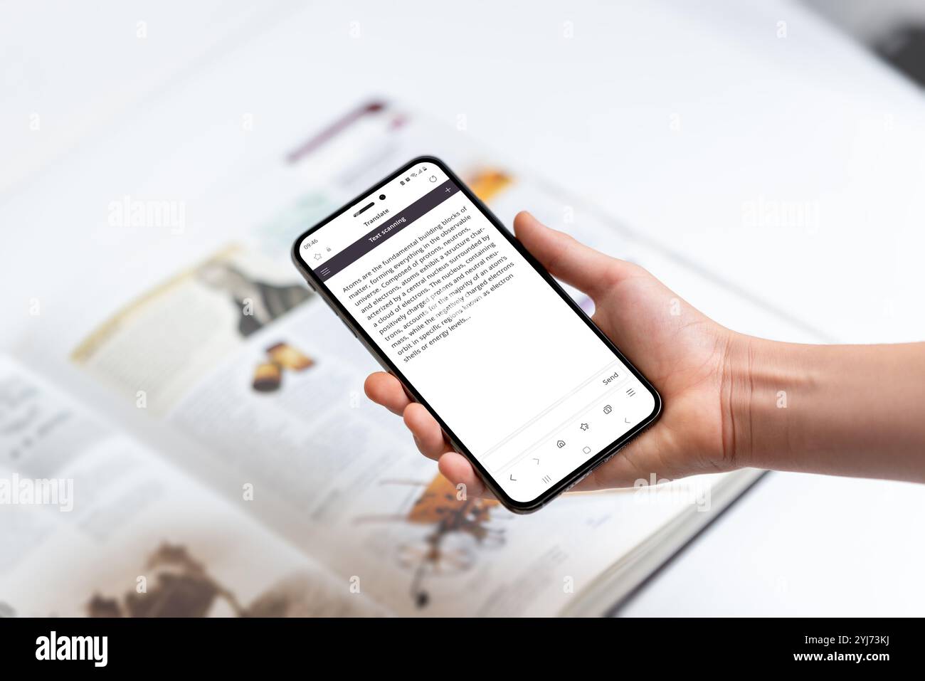 Mano che tiene lo smartphone che scansiona il testo nel libro, che rappresenta l'uso della tecnologia per estrarre conoscenze, informazioni e dettagli da materiali stampati Foto Stock