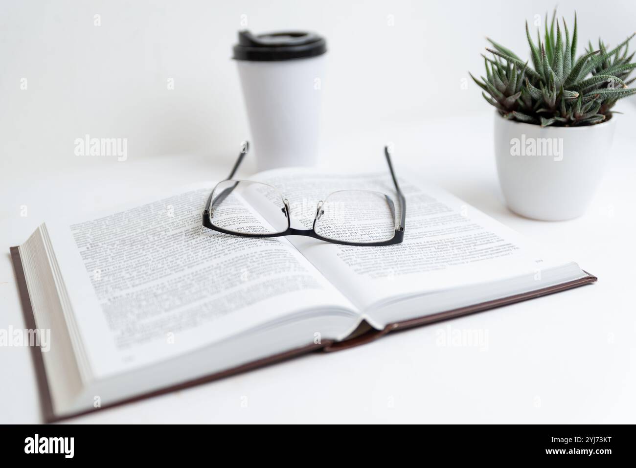 Bicchieri su libro aperto con tazza di caffè e pianta, che simboleggiano un ambiente rilassato di lettura o studio, focalizzatevi sull'apprendimento, un ambiente tranquillo Foto Stock