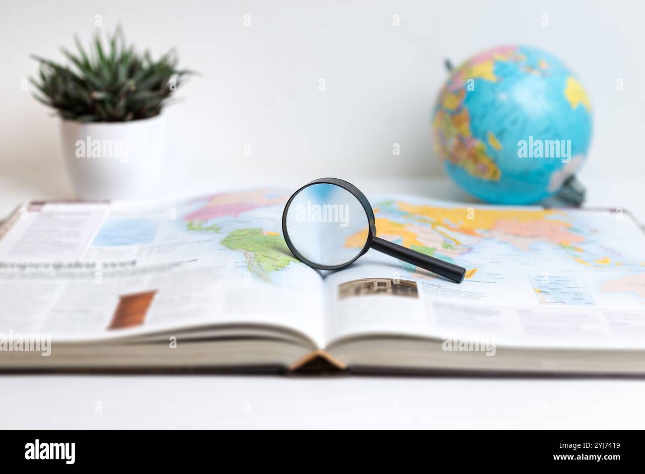 Lente di ingrandimento su un libro aperto che mostra la mappa del mondo con il globo sullo sfondo. Ideale per temi di ricerca globale, viaggi, geografia, esplorazione e. Foto Stock