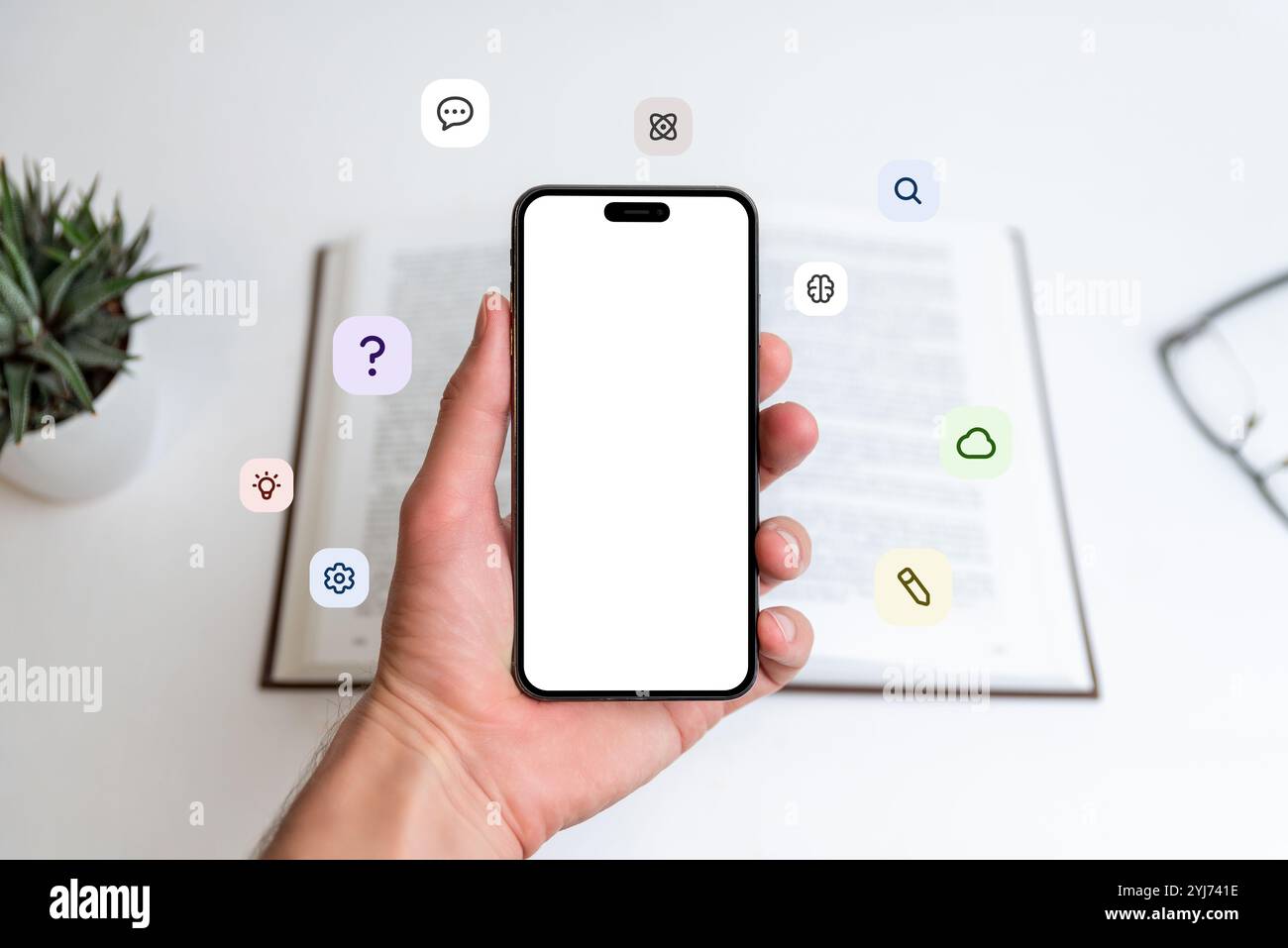 Modello telefonico in mano davanti a un libro aperto con icone volanti: Punto interrogativo, idea, nuvola, penna, atomo, cervello. Ideale per l'apprendimento, la tecnologia e la grafica didattica Foto Stock
