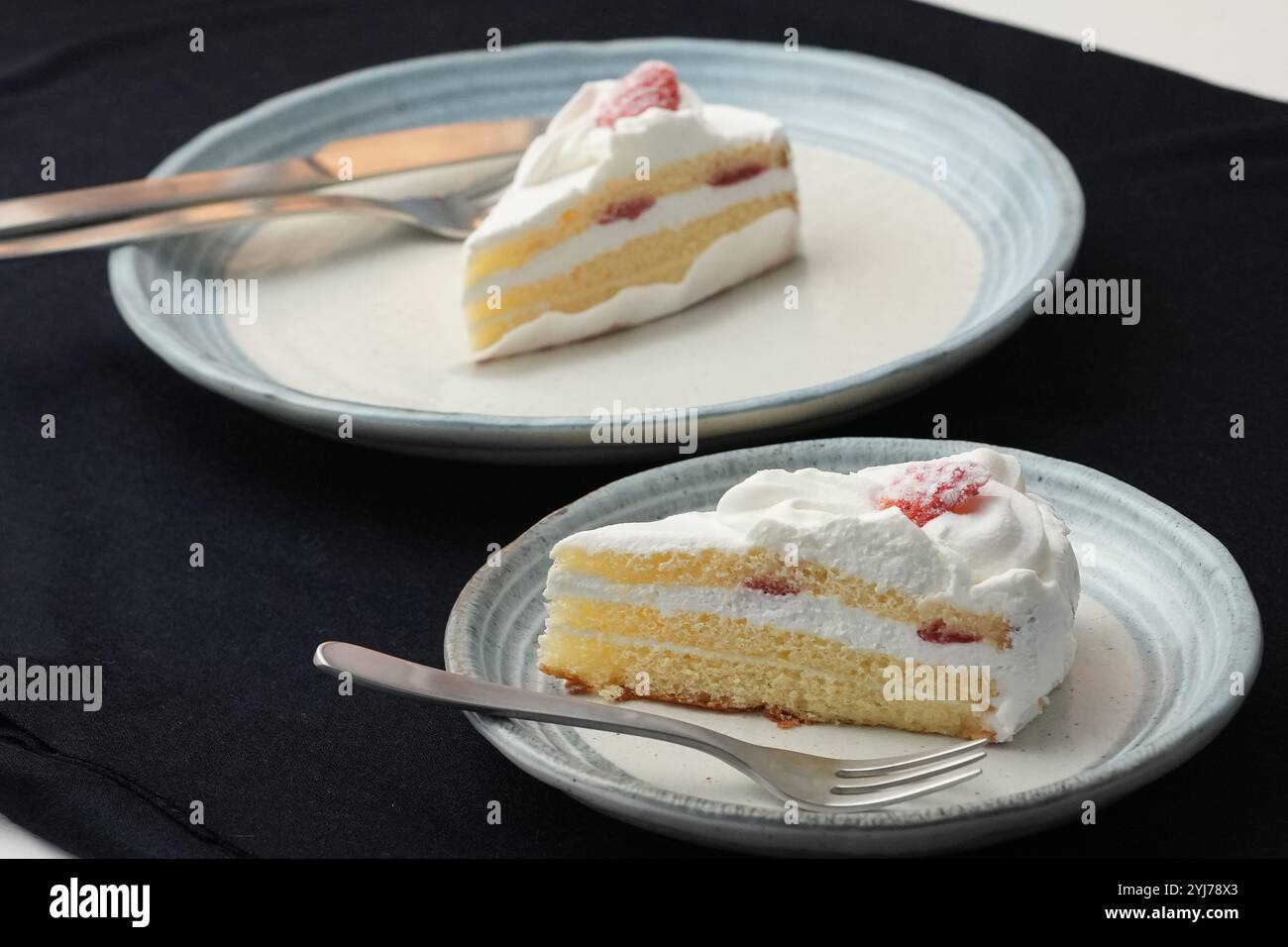 Piccola torta di fragole giapponese, forchetta e coltello ciascuno su due eleganti piatti grandi e piccoli in stile giapponese su un panno nero su un tavolo bianco. Foto Stock