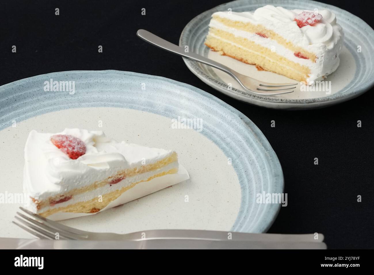 Piccola torta di fragole giapponese, forchetta e coltello ciascuno su due eleganti piatti grandi e piccoli in stile giapponese su un panno nero su un tavolo bianco. Foto Stock