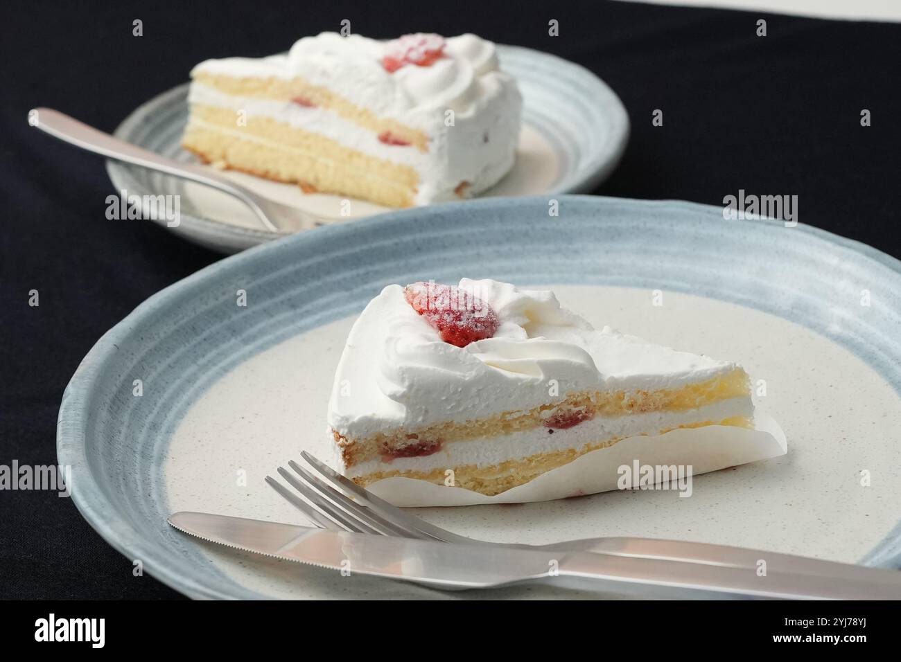 Piccola torta di fragole giapponese, forchetta e coltello ciascuno su due eleganti piatti grandi e piccoli in stile giapponese su un panno nero su un tavolo bianco. Foto Stock