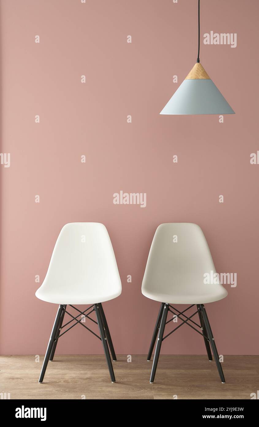Due sedie e lampada a sospensione di fronte alla parete rosa Foto Stock
