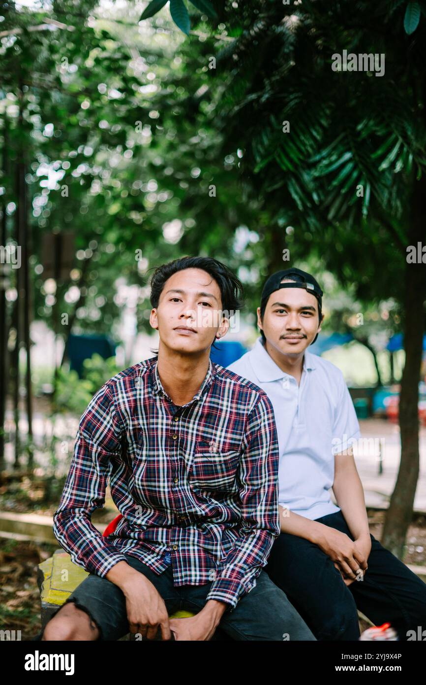 Due uomini del sud-est asiatico seduti in una piazza della città, catturano un momento di relax e conversazione. Ideale per progetti incentrati sulla vita urbana, comuni Foto Stock