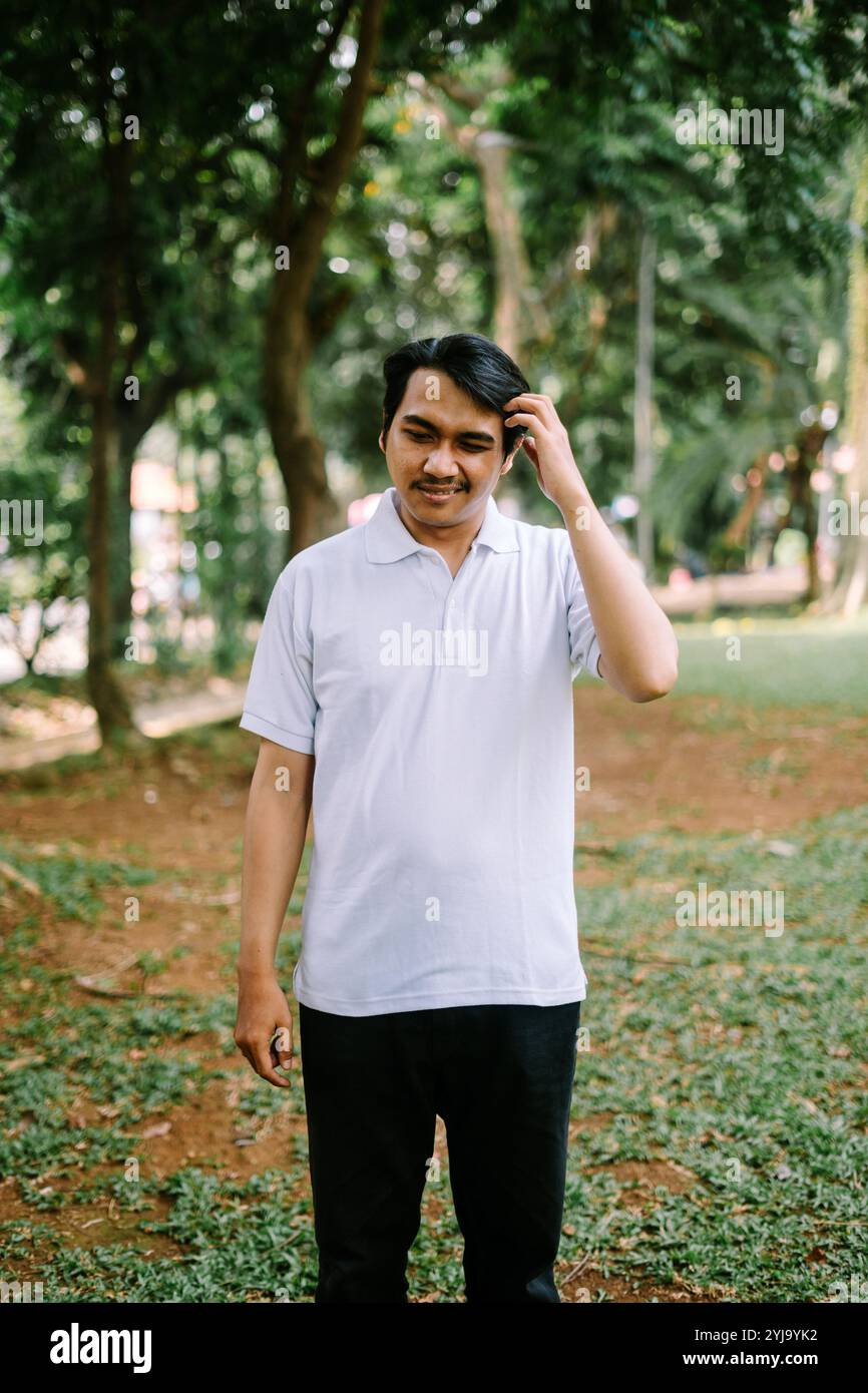 Uomo del sud-est asiatico che tiene la testa, esprime stress o pensiero profondo. Ideale per progetti incentrati su emozioni, contemplazione o momenti difficili Foto Stock