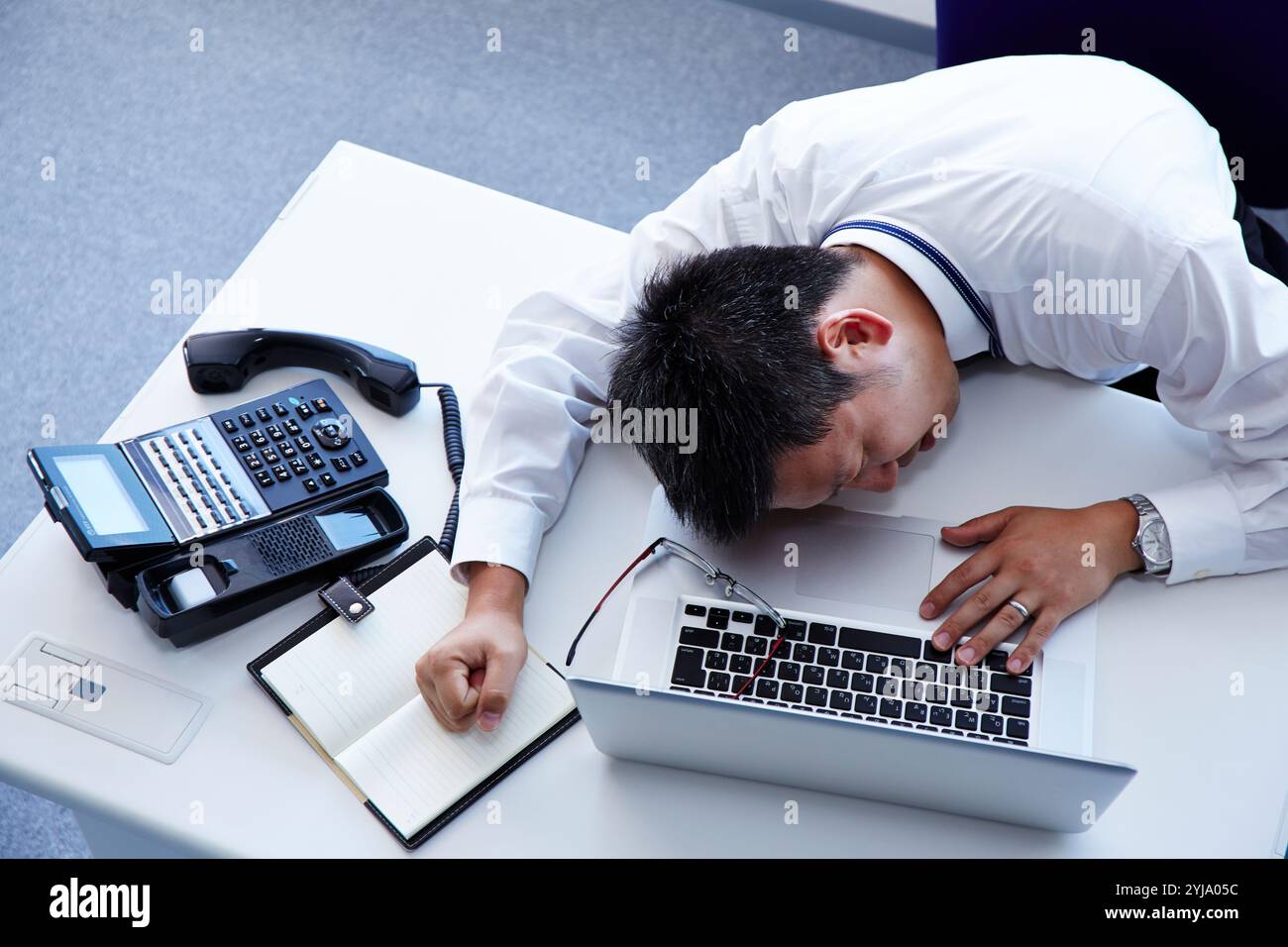 Uomo sdraiato sulla scrivania con espressione dolorosa sul viso Foto Stock