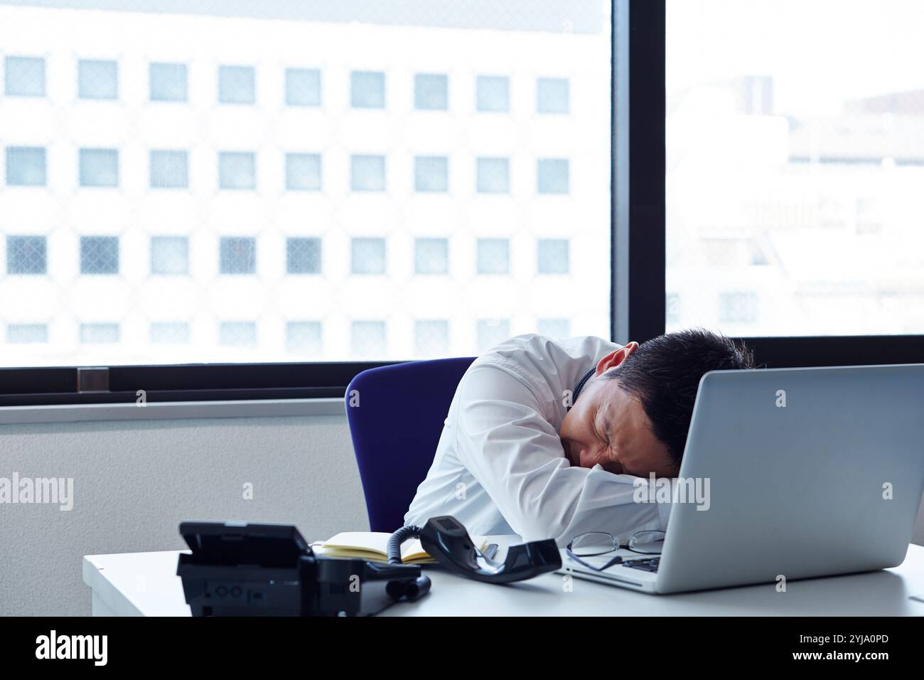 Uomo sdraiato a faccia in giù sulla scrivania con espressione dolorosa Foto Stock