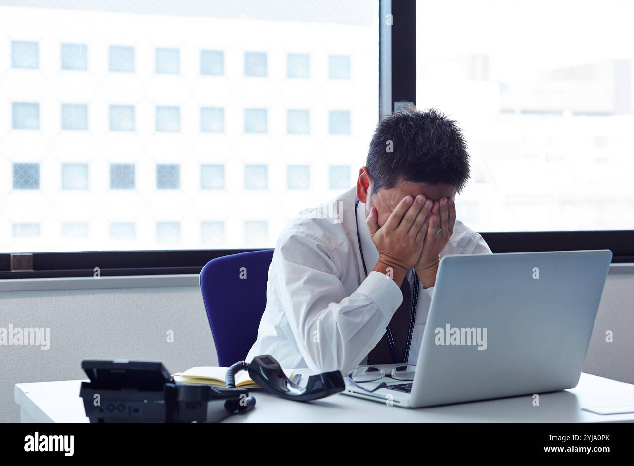 Uomo con il viso coperto e angosciato alla scrivania Foto Stock