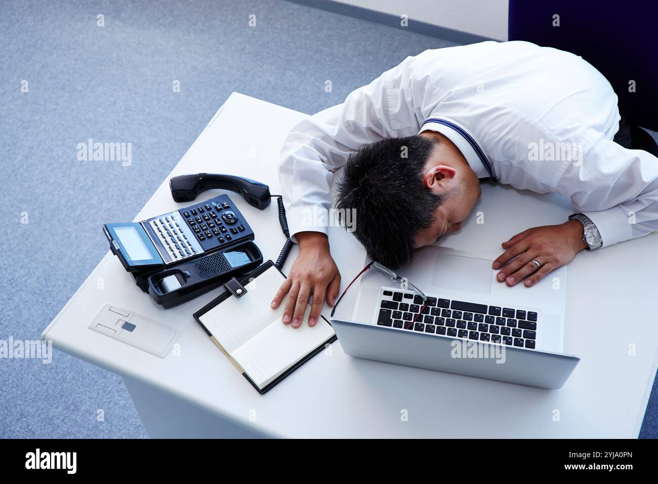Uomo sdraiato sulla scrivania con espressione dolorosa sul viso Foto Stock