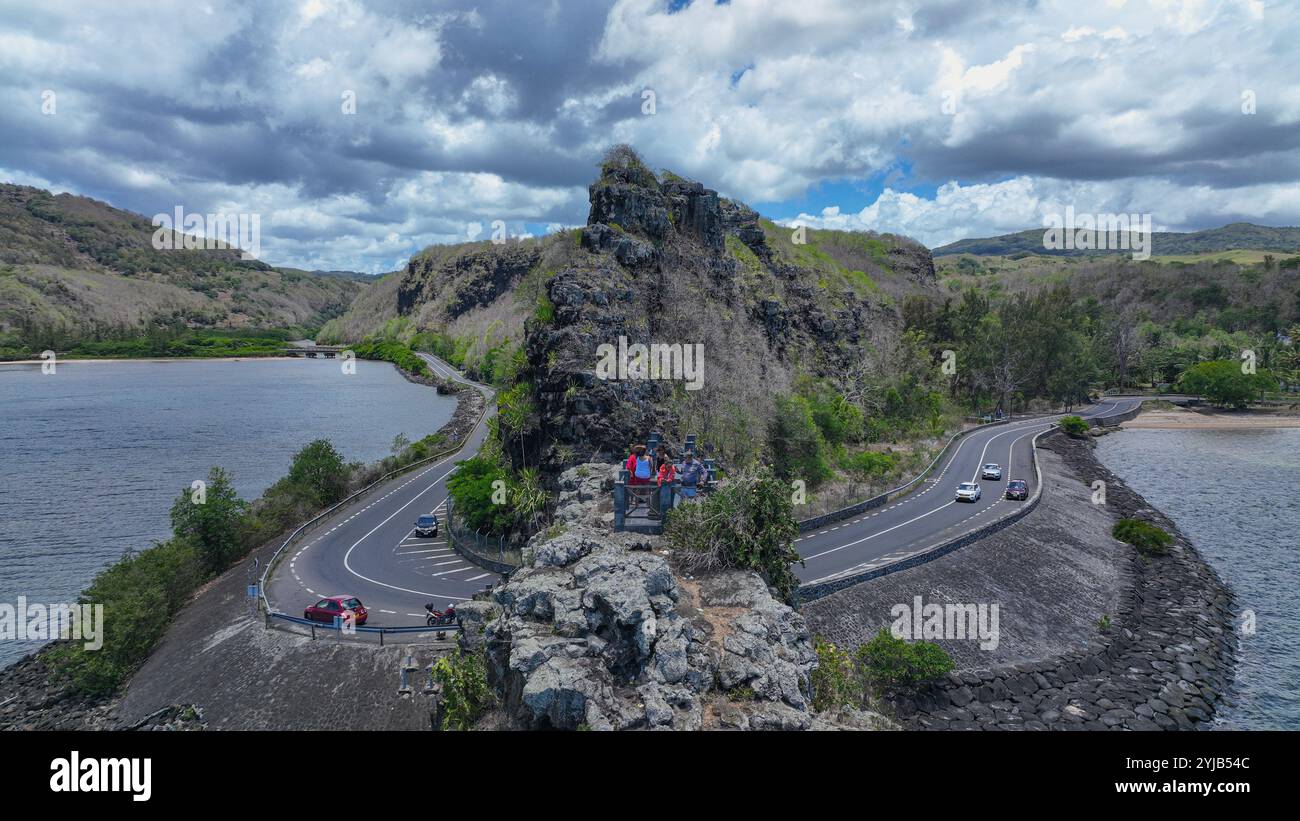 Un gruppo di individui si trova sul lato di una strada vicino a un pittoresco lago di Mauritius. Foto Stock