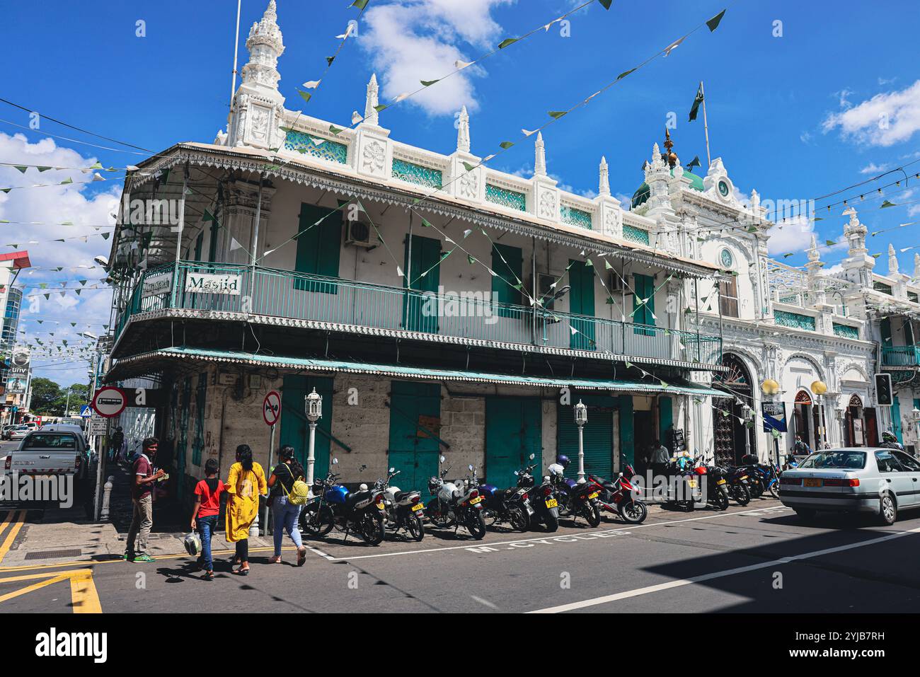 Un gruppo diversificato di individui in piedi di fronte a un edificio, situato nella città di Port Louis, Mauritius, con un'importante moschea sullo sfondo. Foto Stock