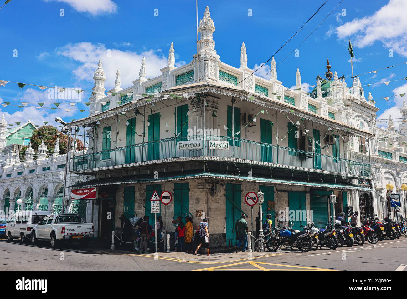 Un gruppo eterogeneo di individui si trova all'esterno di un edificio nella città di Port Louis, Mauritius, con un'importante moschea sullo sfondo. Foto Stock