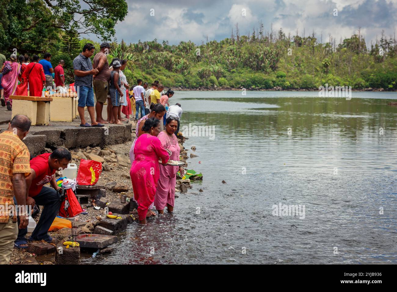 Un gruppo eterogeneo di individui, che rappresentano le tradizioni indiane e la cultura indù, si trova accanto a un corpo d'acqua nelle Mauritius. Foto Stock