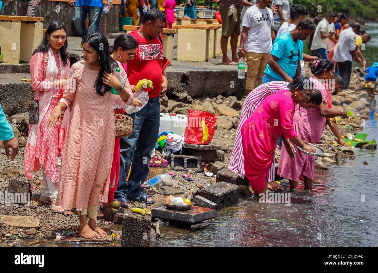 Un raduno di individui delle tradizioni indiane, rivestiti di abbigliamento indù, che si trovano insieme vicino a un corpo d'acqua a Mauritius, impegnati in pubbliche relazioni religiose Foto Stock