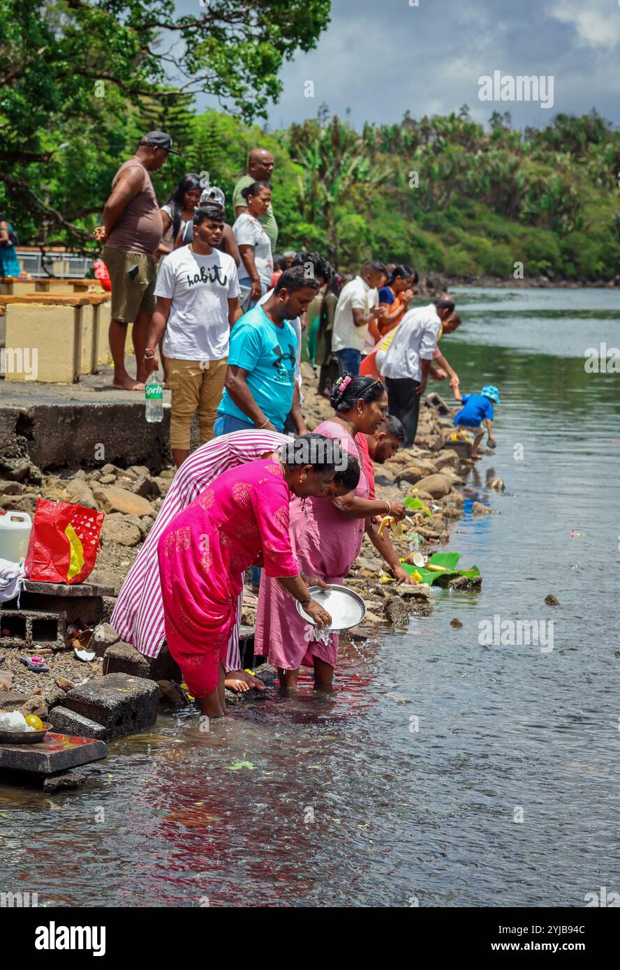 Un gruppo di individui, seguendo le tradizioni religiose indù indiane, che si trovano accanto a un corpo d'acqua nelle Mauritius. Foto Stock