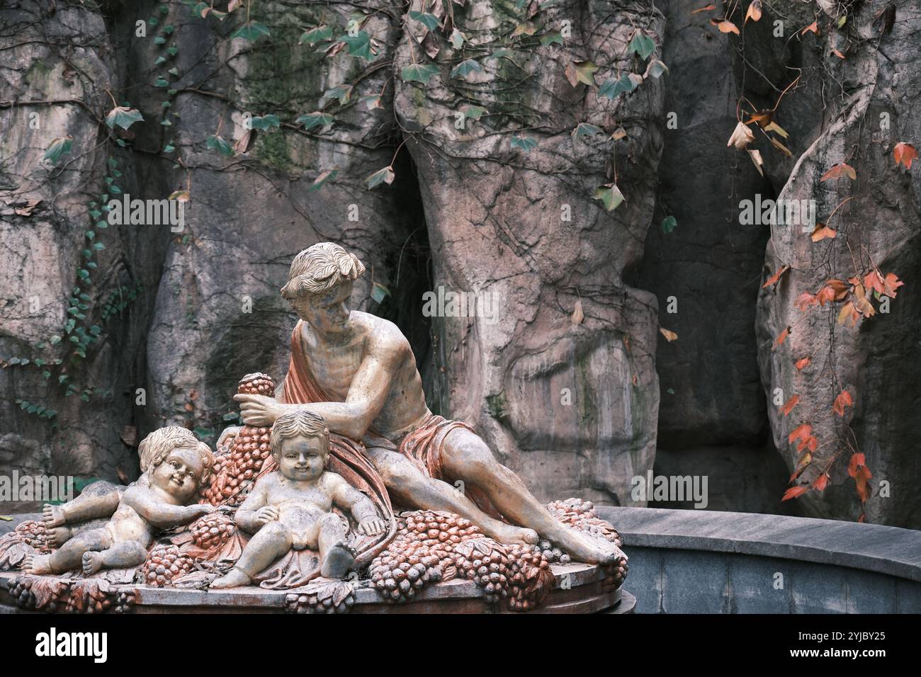 Classica scultura in pietra di un uomo e due cherubini con uva, adagiati su uno sfondo roccioso con viti autunnali. Foto Stock