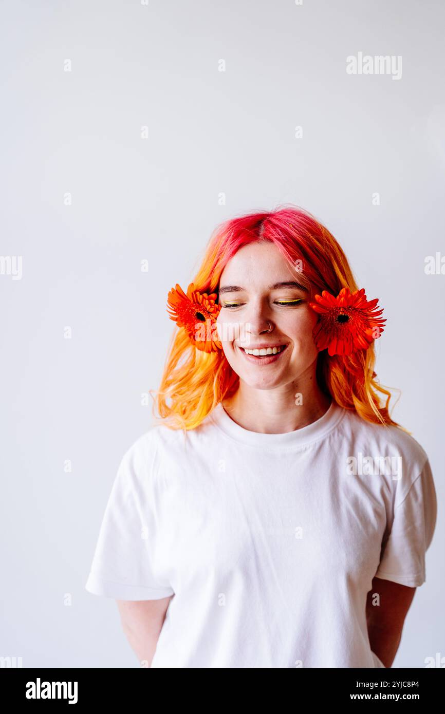 Giovane donna sorridente con capelli rosa e fiori arancioni Foto Stock