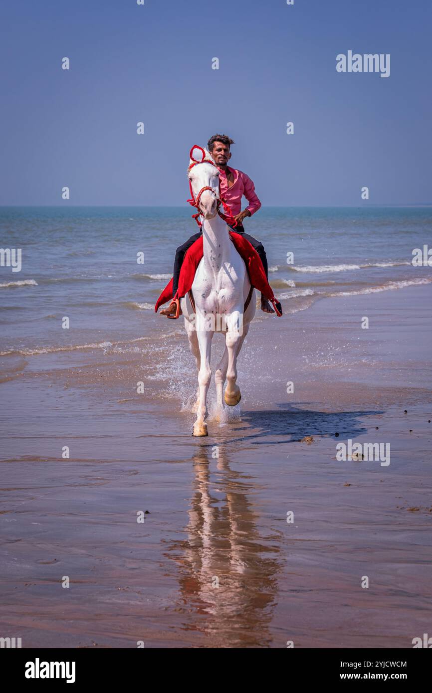 Uomo che cavalca sulla spiaggia di Mandvi, Gujarat, India Foto Stock