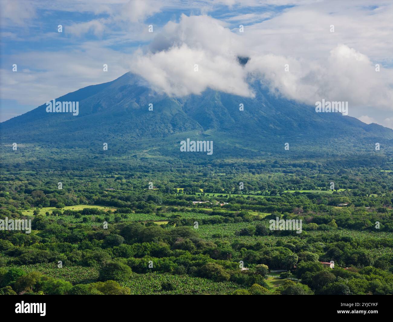 Splendida vista del vulcano circondata da alberi e campi verdeggianti sotto un cielo parzialmente nuvoloso in Nicaragua Foto Stock