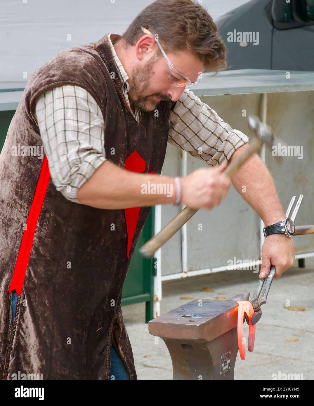 Fabbro con occhiali protettivi che martellano un ferro di cavallo caldo su un'incudine durante una mostra pubblica alle feste di El Cid Burgos Castiglia e Leon Spagna Foto Stock