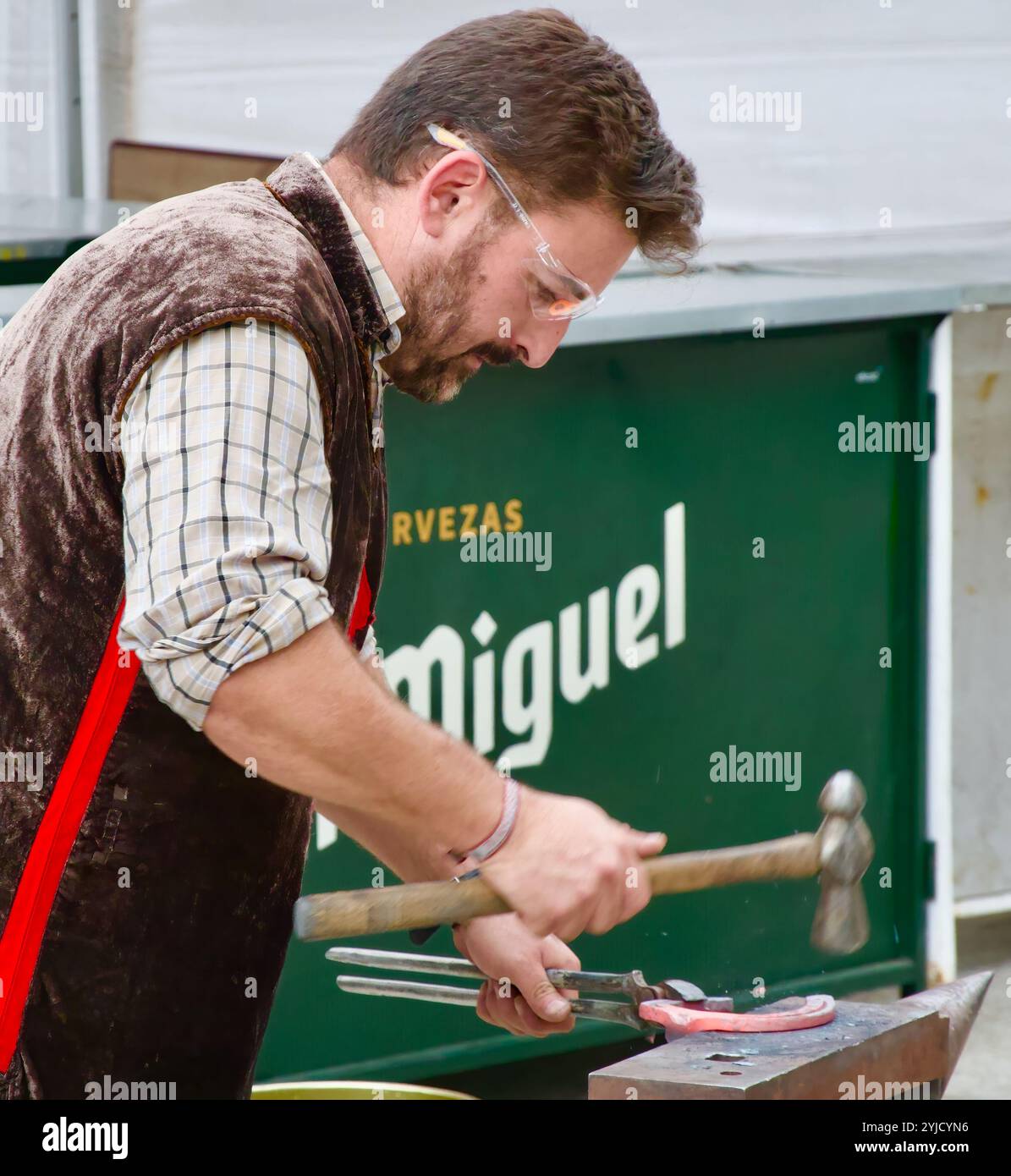 Fabbro con occhiali protettivi che martellano un ferro di cavallo caldo su un'incudine durante una mostra pubblica alle feste di El Cid Burgos Castiglia e Leon Spagna Foto Stock