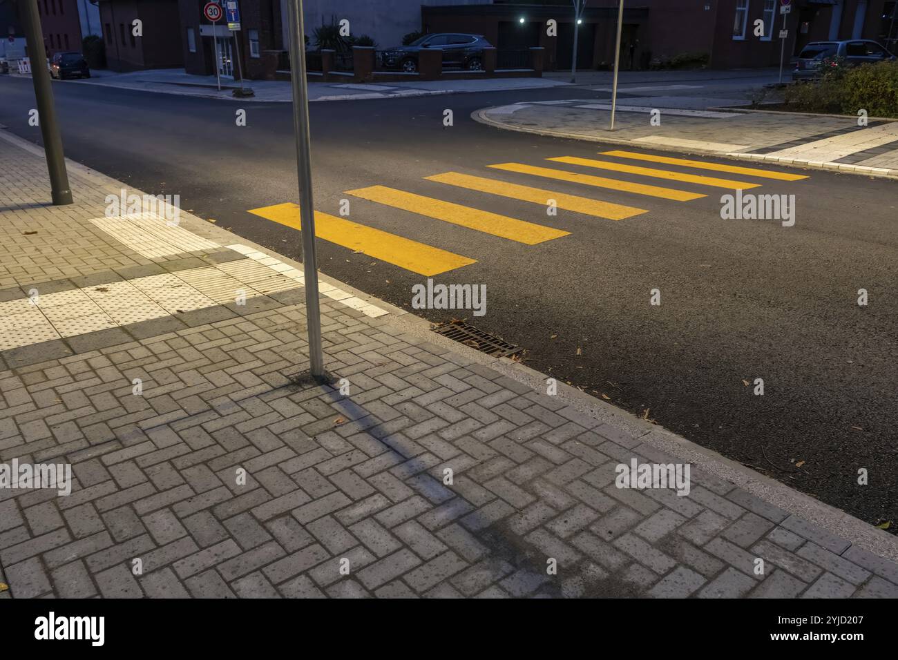 Attraversamento pedonale giallo con pavimentazione tattile su una strada tranquilla al crepuscolo, promuovendo l'accessibilità e la sicurezza stradale Foto Stock