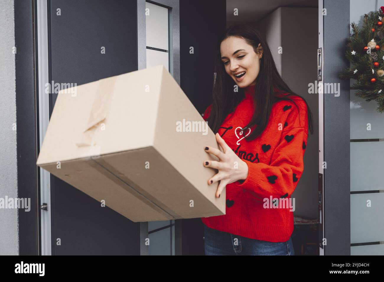 Giovane donna allegra eccitata per un pacco che ha appena ricevuto. Donna che riceve il suo regalo di natale per posta. Aprendo il regalo di Natale a casa Foto Stock