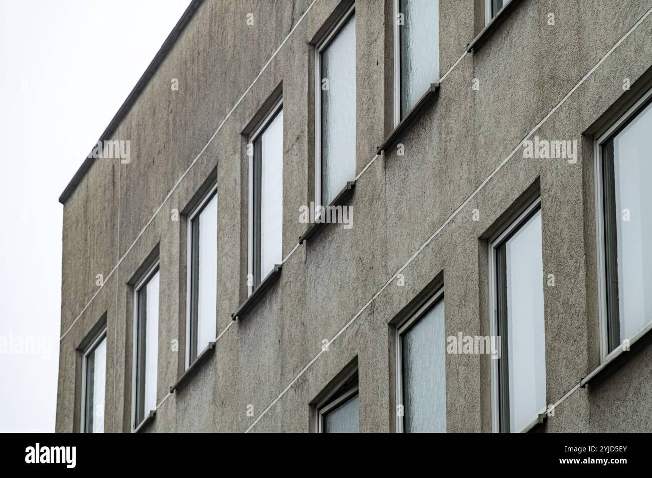 Vista ad angolo basso della facciata grigia in cemento dell'edificio modernista che mostra finestre multiple e linee bianche Foto Stock