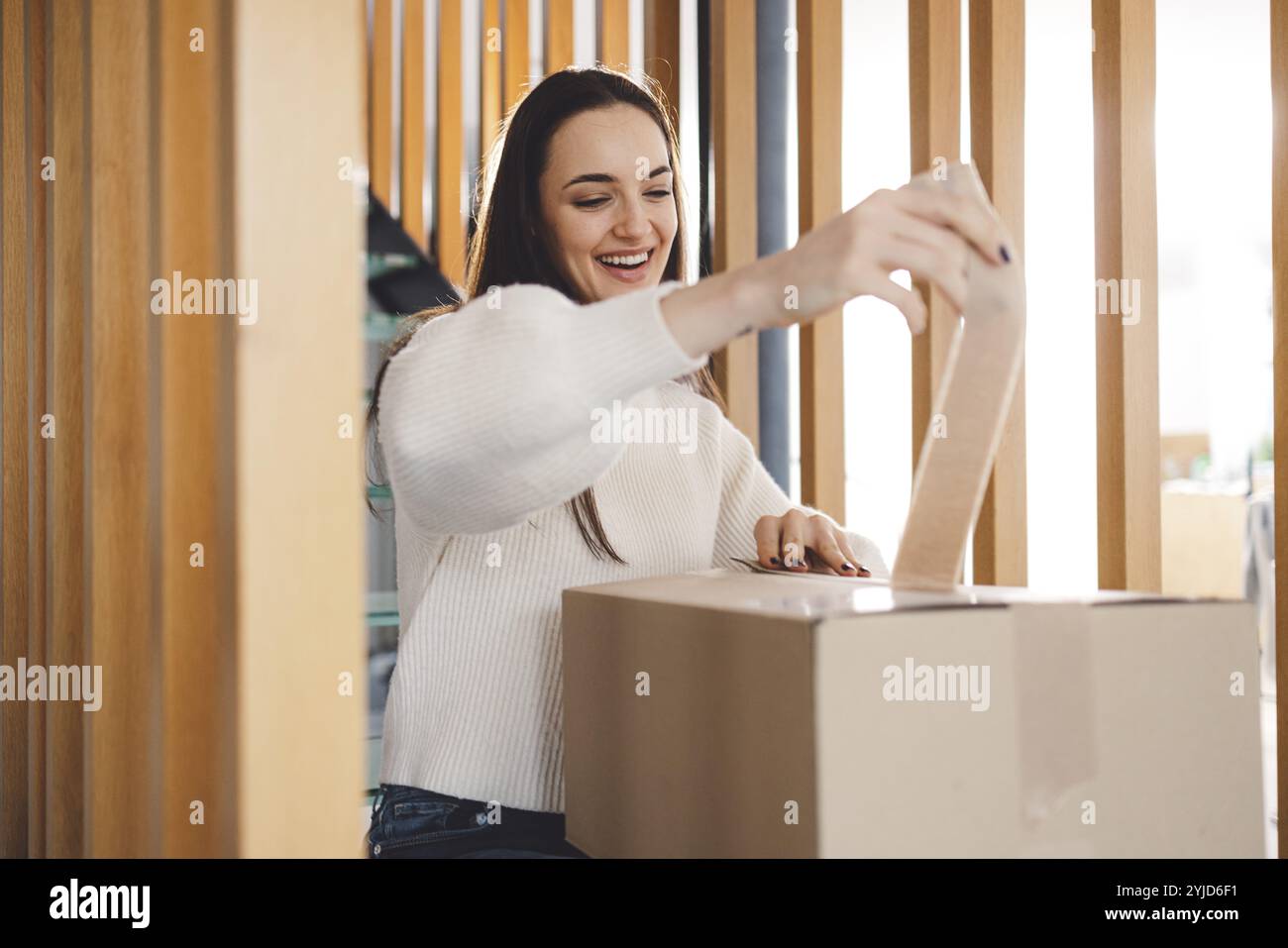 Giovane donna allegra eccitata per un pacco che ha appena ricevuto. Donna che riceve il suo regalo di natale per posta. Aprendo il regalo di Natale a casa Foto Stock