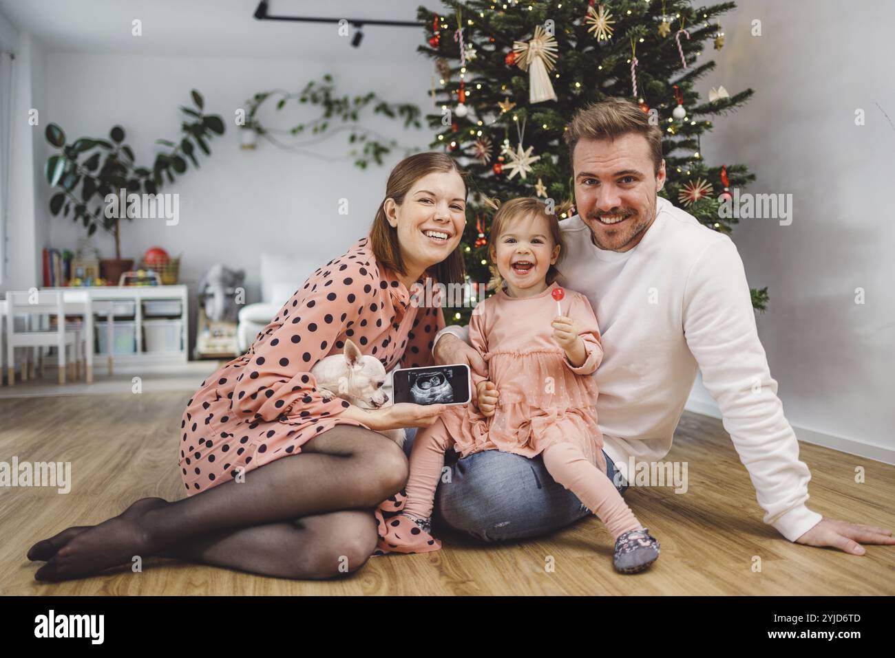 Bellissimo giovane ritratto di Natale della famiglia caucasica. Mamma, papà e una bambina. Mamma e figlia che indossano abiti rosa, papà che indossa un maglione bianco. A. Foto Stock