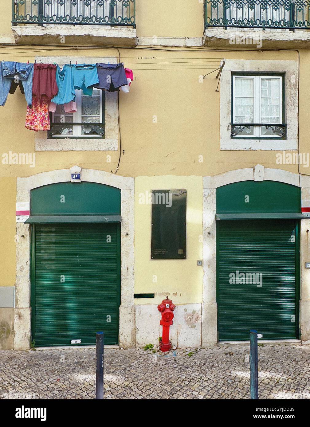 Abiti appesi sulla facciata dell'edificio sopra due porte verdi con persiane, Lisbona, Portogallo Foto Stock