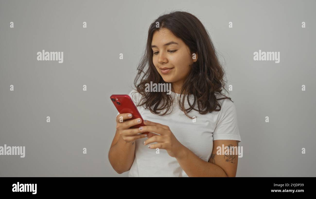 Attraente giovane donna bruna ispanica che usa uno smartphone, isolata su un muro bianco. Foto Stock