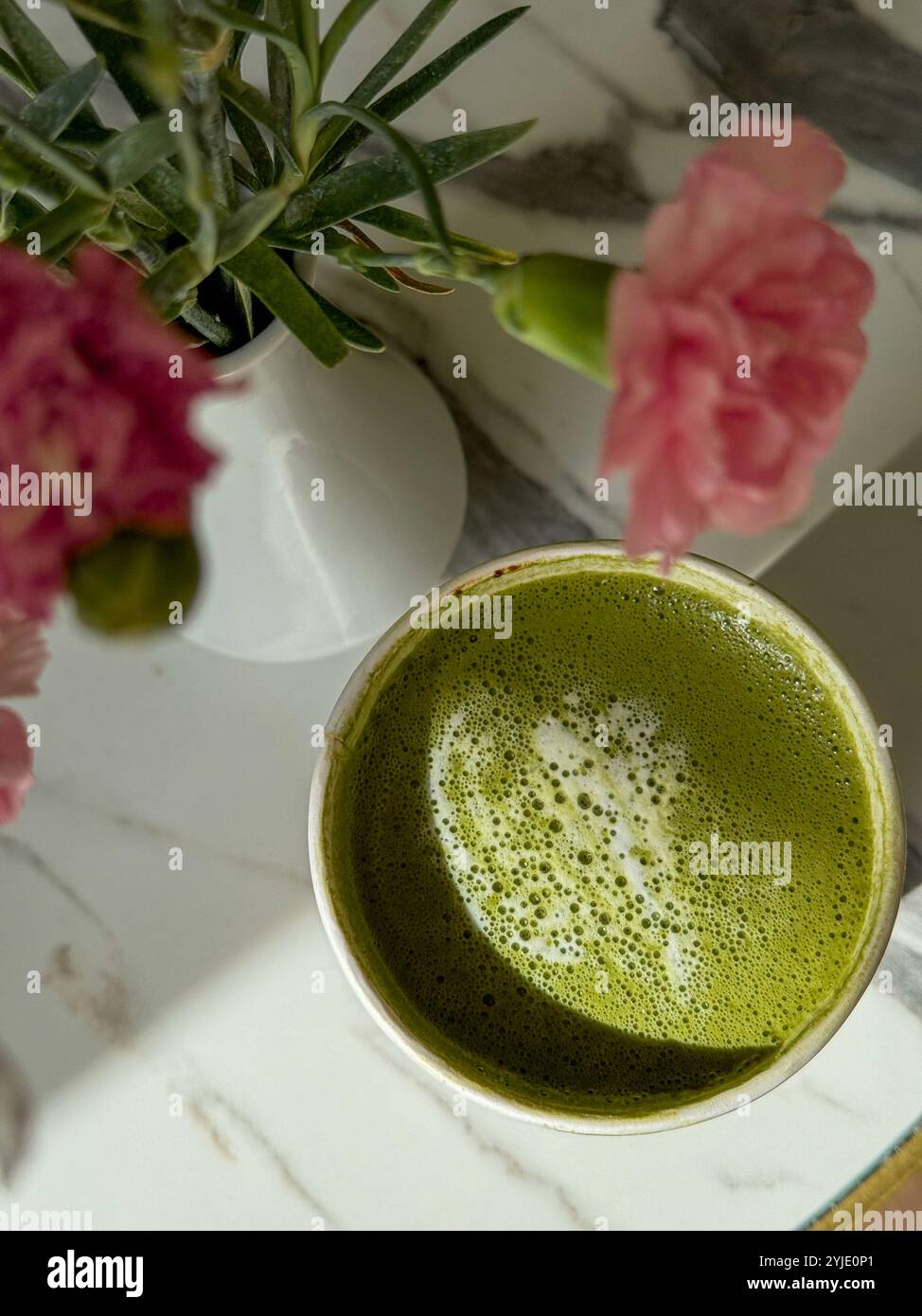 Una bella tazza di tè matcha con fiori rosa freschi su un tavolo di marmo Foto Stock