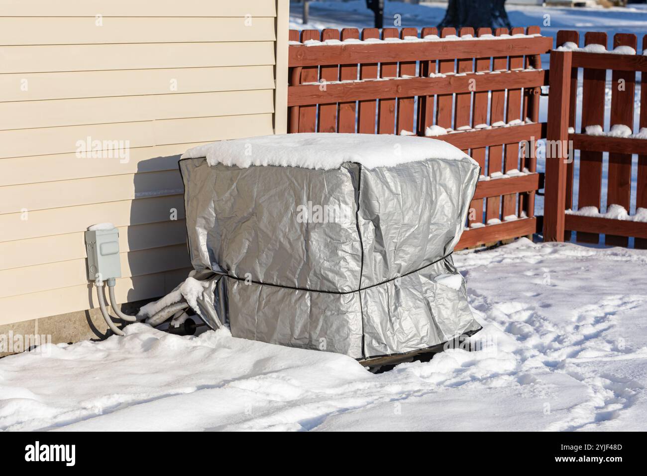 Climatizzatore casa con copertura protettiva e neve durante l'inverno. Climatizzazione domestica, HVAC, manutenzione, inverno e concetto di manutenzione. Foto Stock