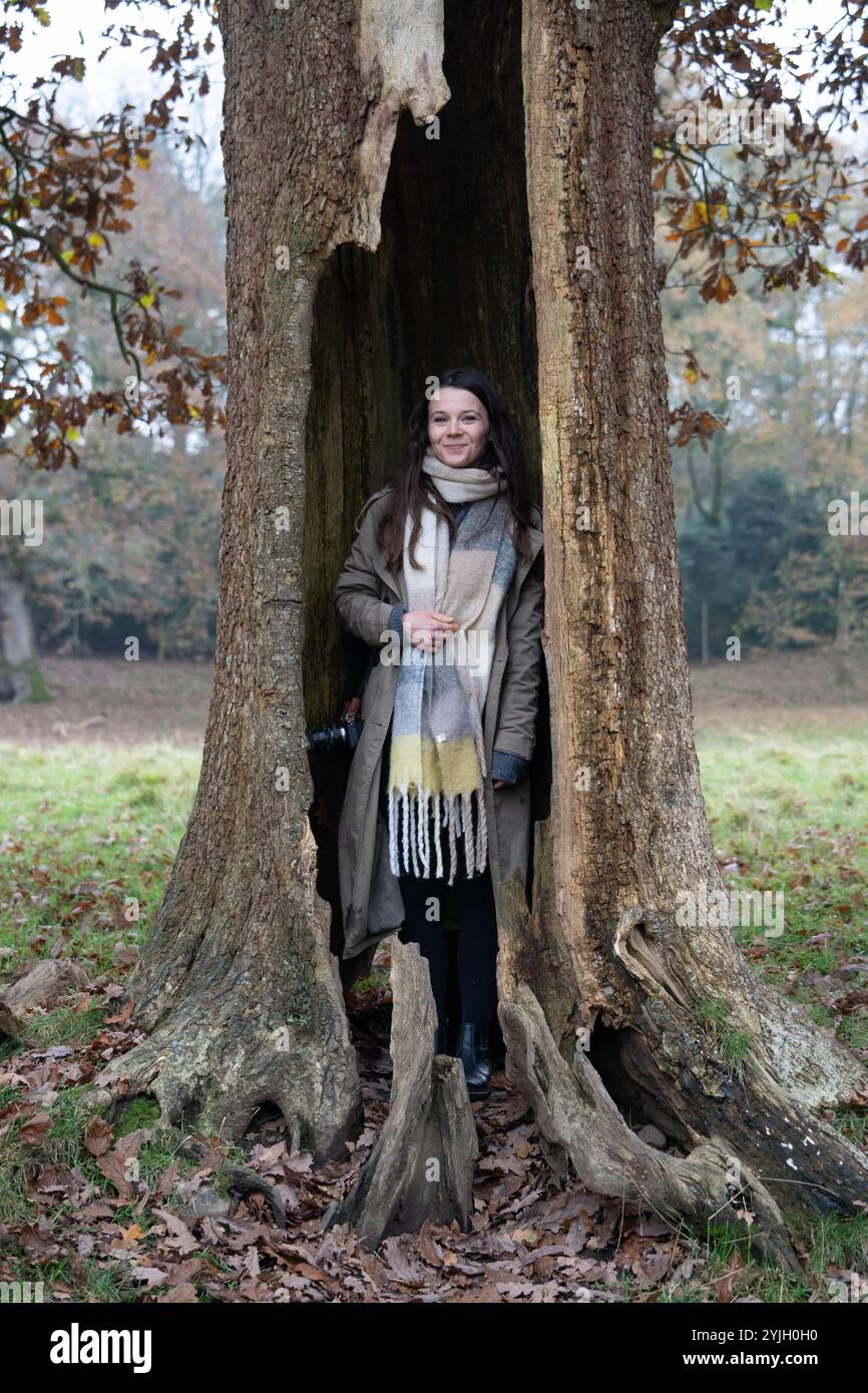 Donna in piedi all'interno di un tronco di alberi cavi nella campagna autunnale del Lake District Foto Stock