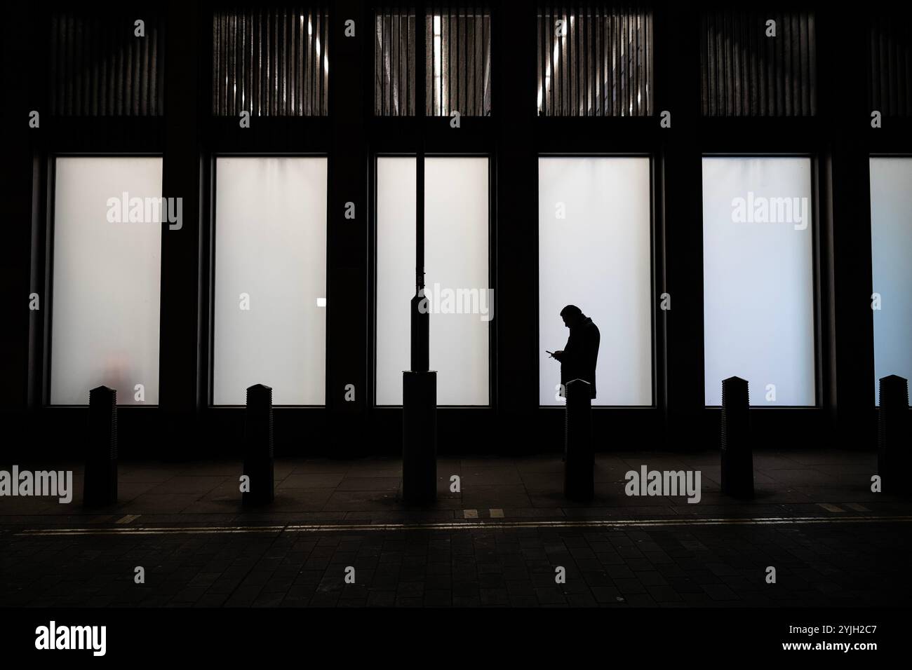 Un operaio di città con il suo smartphone si staglia nella finestra di un edificio commerciale nel cuore della City di Londra, Inghilterra, Regno Unito Foto Stock