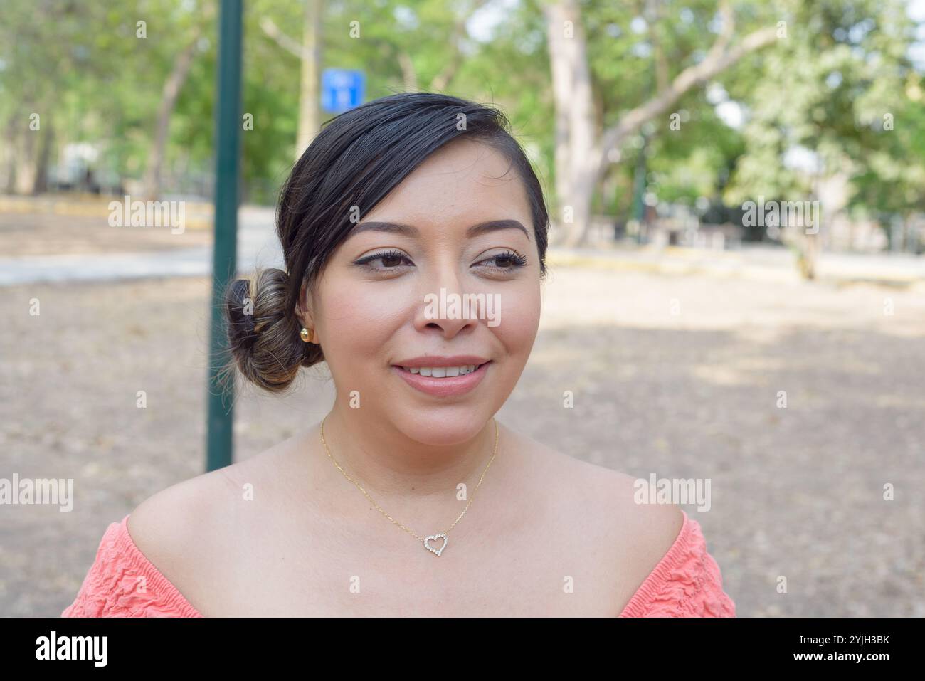 Una giovane donna con i capelli tirata indietro in un panino sorride brillantemente, indossando un top rosa a spalla. Foto Stock