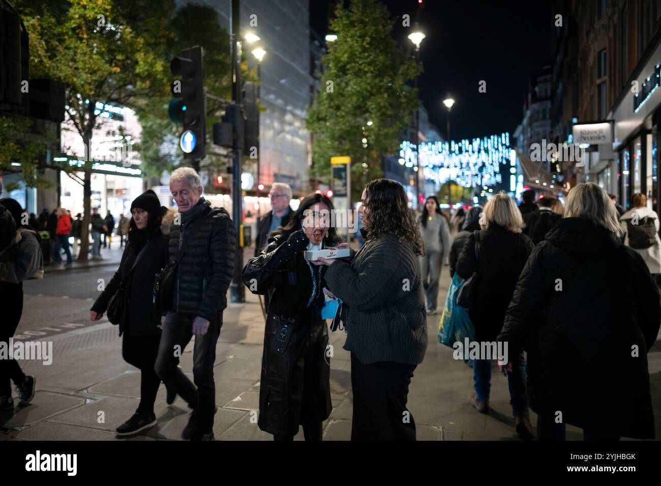 Una donna prende un boccone del suo pasto fast food mentre è in viaggio, Oxford Street, centro di Londra, Inghilterra, Regno Unito Foto Stock