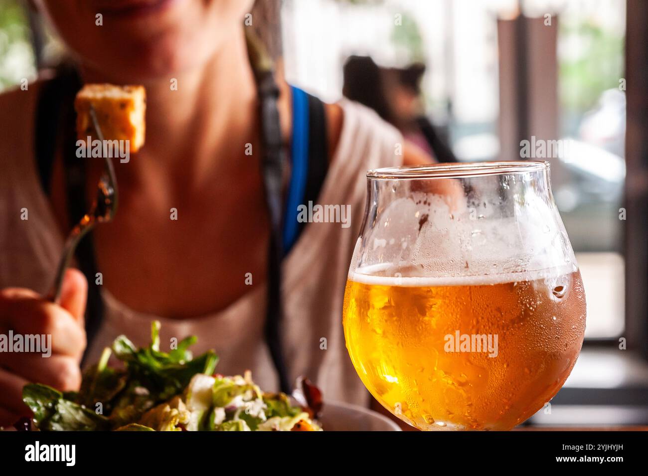 Primo piano di un bicchiere di birra con una donna sfocata sullo sfondo. Foto Stock