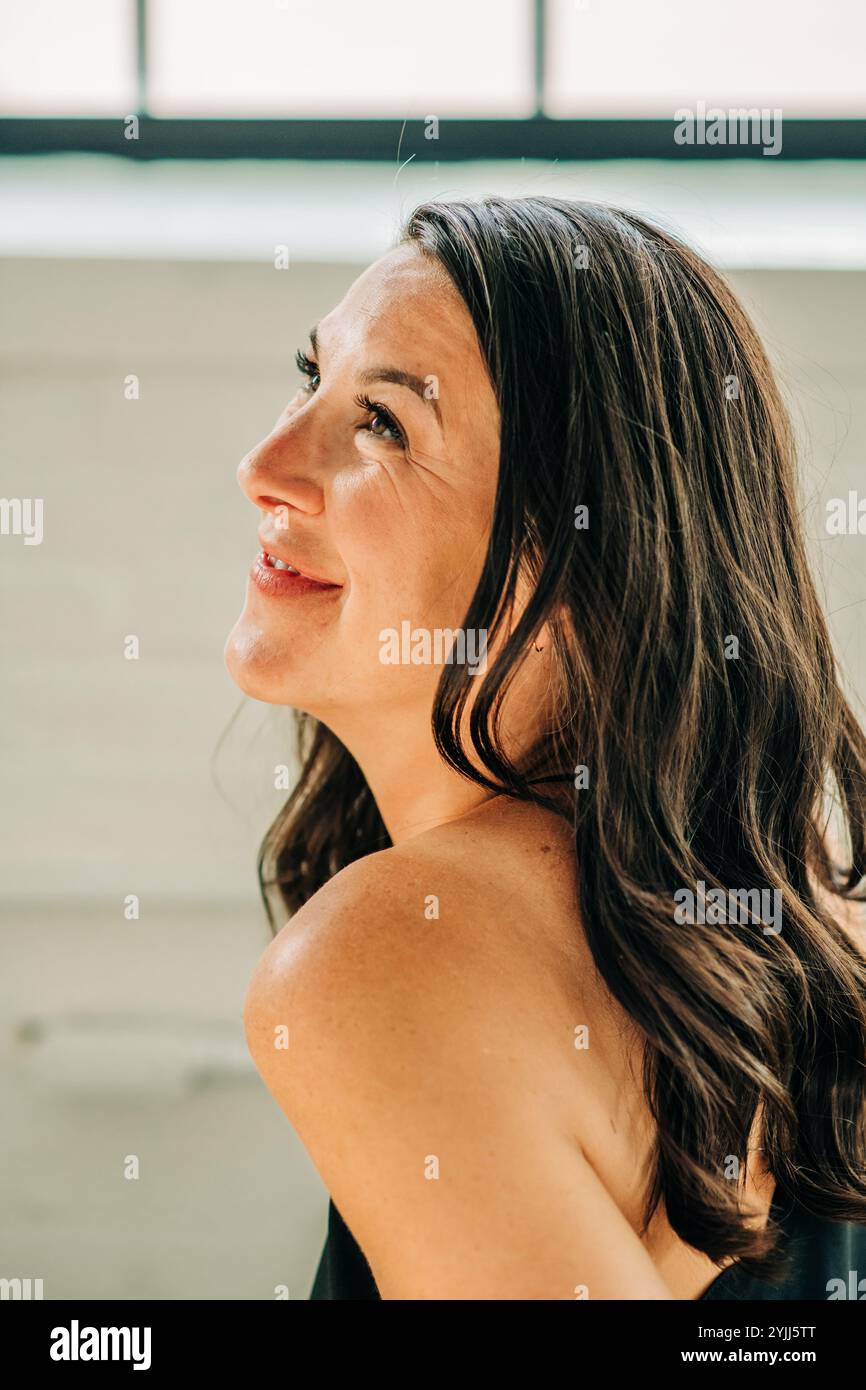 Donna che guarda verso l'alto con un sorriso morbido, catturata dalla luce naturale Foto Stock