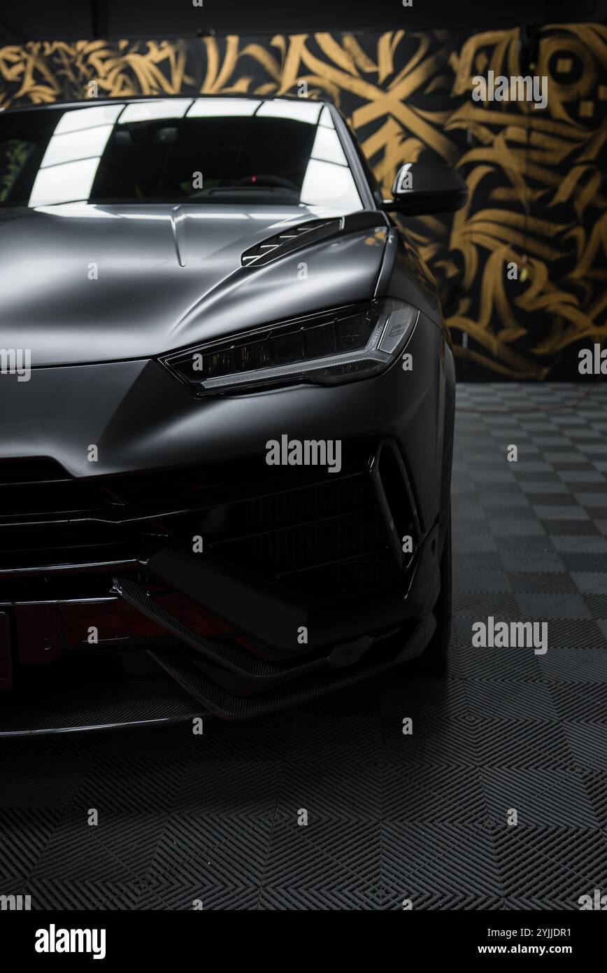 Parte anteriore della Lamborghini Urus Performante all'interno su un piano a scacchi. Il murale astratto nero e oro sullo sfondo evidenzia la finitura opaca dell'auto. Foto Stock