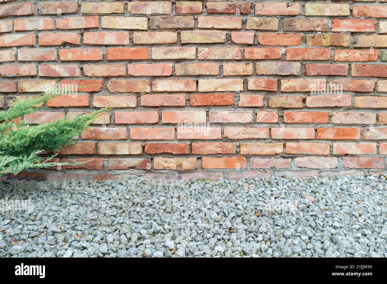 Muro in mattoni rossi con piante verdi e ghiaia in primo piano Foto Stock