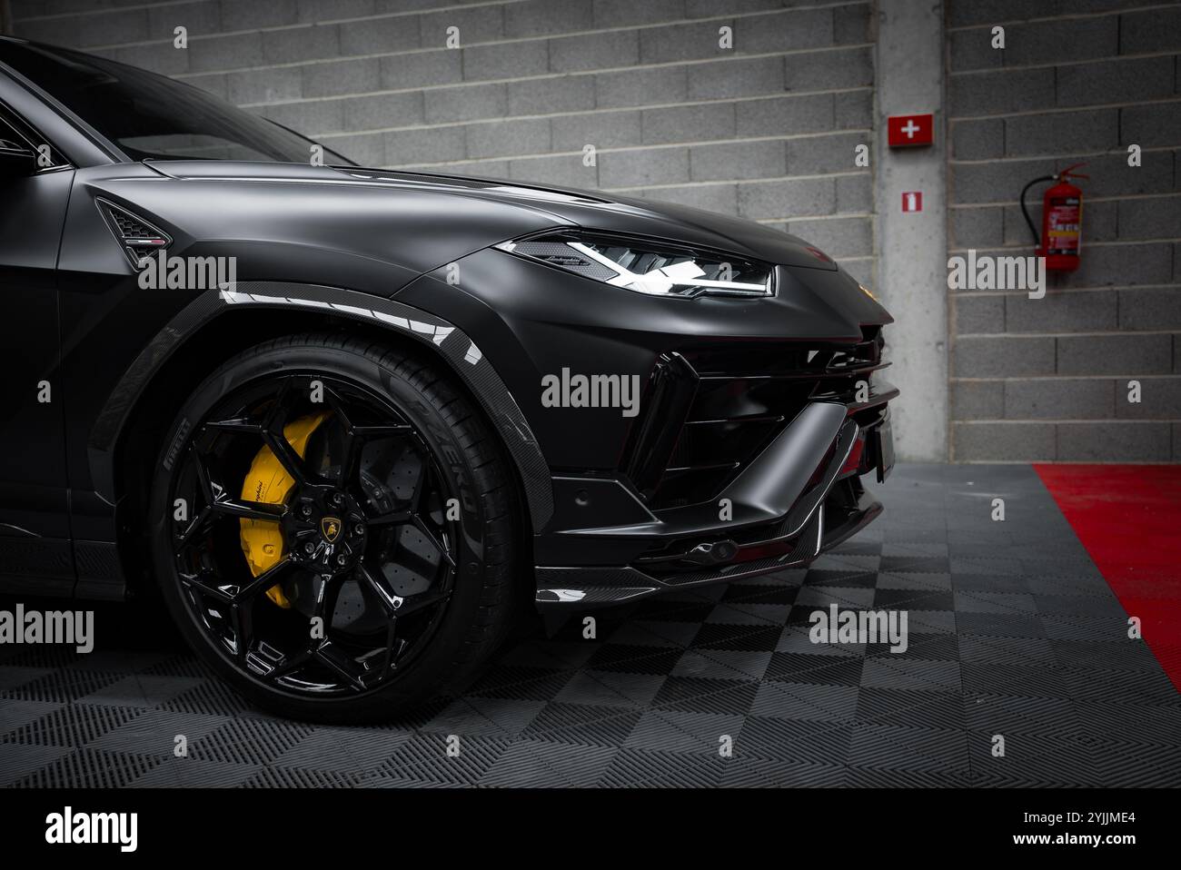 Sezione anteriore della Lamborghini Urus performante con finitura nera opaca, cerchi neri e pinze dei freni gialle in uno showroom con parete in mattoni grigi. Foto Stock