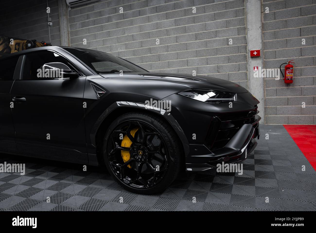 L'immagine presenta una Lamborghini Urus Performante nera opaca, che si concentra sulla sua sezione anteriore con linee nette, parcheggiata all'interno su un pavimento a scacchi. Foto Stock