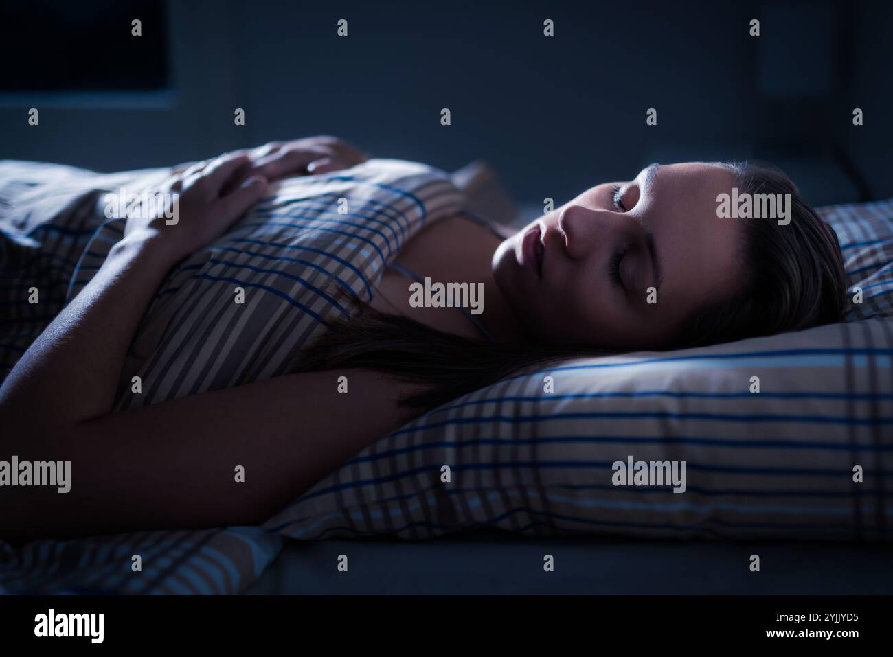 Donna addormentata a letto di notte. Bel sogno dopo la melatonina. REM. Profondo Ragazza nella camera da letto buia. Cuscino e piumone. Faccia alla luce. Riposati in una camera accogliente. Foto Stock