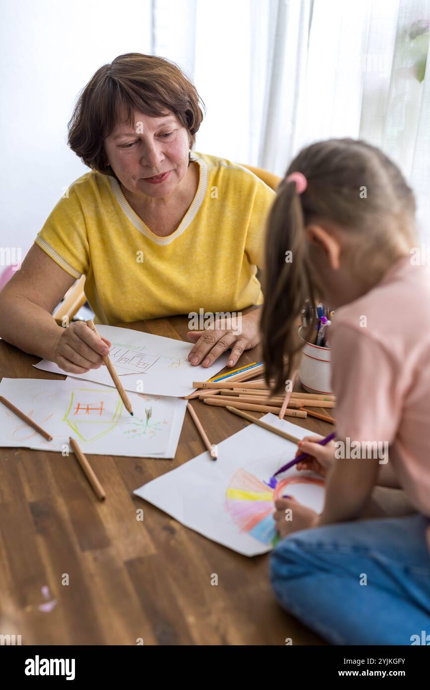 Nonna e nipote creano felicemente arte insieme a matite colorate, godendosi il loro tempo. Foto di alta qualità Foto Stock