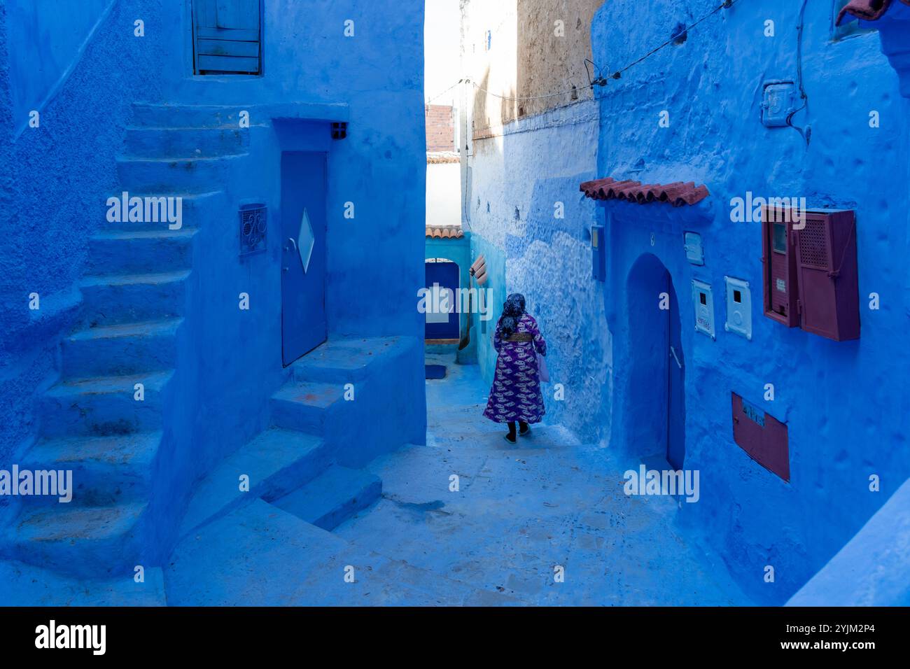 Una donna irriconoscibile in abito tradizionale che cammina in un vicolo dipinto di blu a Chefchaouen, in Marocco. Foto Stock