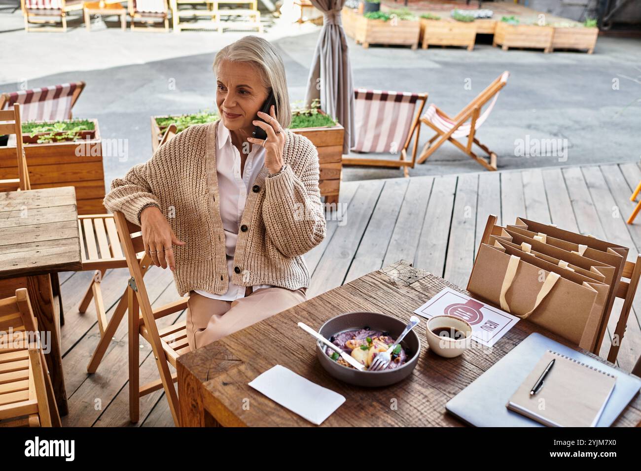 Una bella donna matura si impegna in una piacevole conversazione telefonica mentre si gusta il suo pasto. Foto Stock